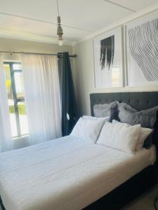 een slaapkamer met een bed met witte lakens en ramen bij Lethabo Eco_Estate in Boksburg