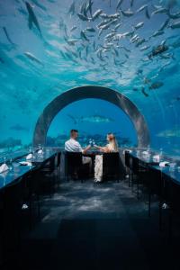 a couple sitting at a table in front of an aquarium at You & Me Maldives in Raa Atoll