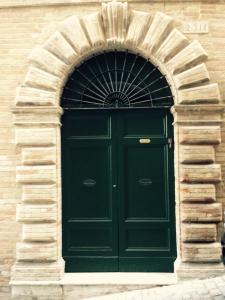 a green door in a stone building with an arch at B&B Antica Biblioteca in Fermo