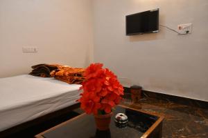 1 dormitorio con 1 cama y un jarrón con flores rojas en Paradise Inn, en Jasidih