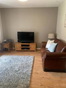 a living room with a brown leather couch and a television at Central 3 Bedroom Townhouse in Wick