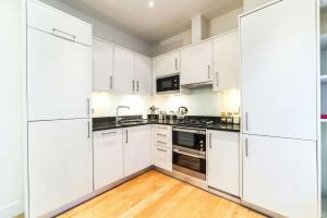 a white kitchen with white cabinets and a wooden floor at StayInn Aldgate East in London