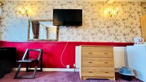 a room with a red wall with a television and a dresser at The Columbia Hotel in Wellingborough