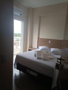 een slaapkamer met een bed met witte lakens en een raam bij Hotel Mãe Peregrina in Aparecida