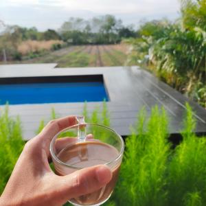 a hand holding a glass of wine in front of a field at ฺBaannoi in the garden บ้านน้อยกลางทุ่ง Pool villa 