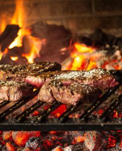 deux morceaux de viande sur un grill avec flammes dans l'établissement Bungalows Sol y Mar, à Canoas de Punta Sal