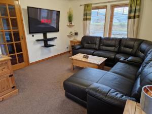 sala de estar con sofá de cuero negro y TV de pantalla plana en Mountain View No12, en Aviemore