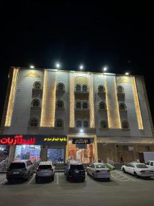 un grand bâtiment avec des voitures garées dans un parking dans l'établissement هابي دريم للشقق المخدومة, à Ukaz