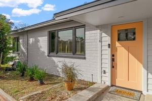 uma casa branca com uma porta laranja e plantas em Smart Bungalow: 10-min to UF, Central Location em Gainesville