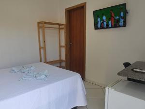 um quarto com uma cama com um lençol branco e uma televisão em Pousada Casa Bella em Itaberaba