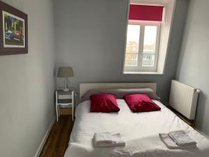 a bed with two red pillows and a window at Maison entière proche tram 170 m2 jardin parking in Marcq-en-Baroeul
