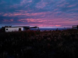 un edificio en medio de un campo con una puesta de sol en Casa de madera en playa de Cabo Polonio con dos ambientes, en Cabo Polonio