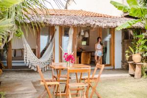 a woman standing outside of a house with a table and chairs at Casa PESQUEIRA Preá - Frente Mar! in Prea