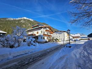 ein Haus auf einer schneebedeckten Straße mit einem Berg in der Unterkunft am Mühlbach - Pension Luttinger in Bichlbach