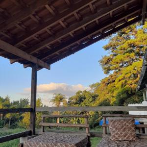 un banc en bois assis sur une terrasse couverte avec des arbres en arrière-plan dans l'établissement Embu Manacás da Serra, à Embu