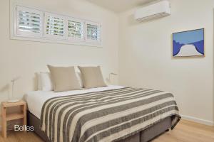 a white bedroom with a bed with a striped blanket at Bluewater on the Beach in Byron Bay