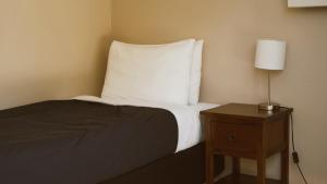 - un lit avec un oreiller blanc et une table avec une lampe dans l'établissement The Barn Cabins & Camp, à Marahau