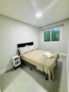 a white bedroom with a bed and a window at Estadia perfeita em Florianópolis: Apartamento com 2 Quartos, 1 Suíte e Churrasqueira no Ribeirão da Ilha - Uma Oportunidade Imperdível in Florianópolis
