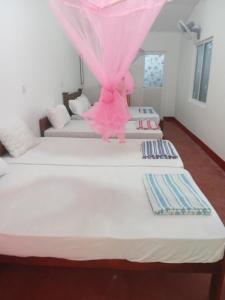 um quarto com três camas com um vestido rosa em Vibushan Guest House em Nilaveli