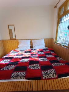 a bed with a red and black quilt on it at OYO Banka Guest House in Manāli