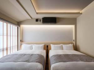 two beds in a room with a tv on the wall at Hotori Machiya House in Kanazawa