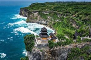 an island with a building on a cliff next to the ocean at Roejas Sunset in Uluwatu