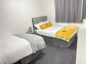 two beds with yellow pillows in a bedroom at Hometel Digs Hidden Gem Large Comfy Home Can Sleep 15 in Braunstone