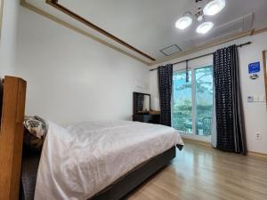 a bedroom with a bed and a large window at Wind Jeju Cafe & Pension in Seogwipo