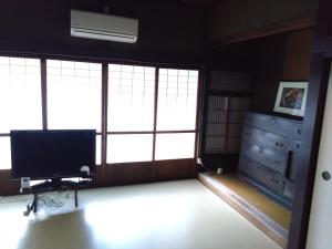 a room with large windows and a television and a dresser at ゲストハウス　シン熊野 in Tanabe