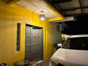 a yellow building with a door and chairs next to a car at VILLA SERI MUTIARA in Kuah
