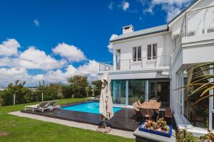 a white house with a swimming pool and an umbrella at White House on Kingswood Golf Estate in George