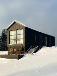 a black building with two chairs in the snow at Ragnar Glamp Milzkalne Lux in Rauda