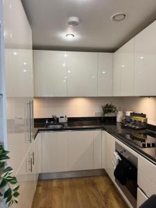 a kitchen with white cabinets and black counter tops at Luxe Lodge Woolwich Arsenal in Woolwich