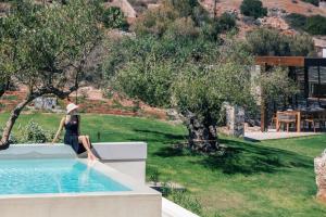 a woman sitting on a wall next to a swimming pool at Villa Katy in Agios Nikolaos