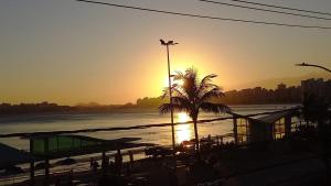 un tramonto su una spiaggia con una palma e l'oceano di Apartamento BEIRA MAR TOTAL-PÉ NA AREIA -VISTA TOTAL PARA O MAR - ÁREA DE CHURRASCO PRIVATIVA- TODAS TVS SMART- MÁQUINA DE CAFÉ -AIR FRYER -NETFLIX -DISNEY PLUS -STARMAX- HBO MAX ASSINADOS - JOGOS- FIRE TV STICK AMAZON- GELADEIRA EXTRA PARA BEBIDAS a Guarapari