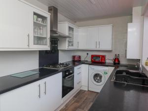 cocina con armarios blancos, lavadora y secadora en The Old Smithy en Morpeth
