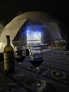 two glasses of wine on a table with a bottle of wine at Glamping Dream Domes Ismayilli in İsmayıllı