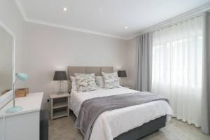 a white bedroom with a bed and a window at Modern 1 bedroom non-seafacing unit on luxury golf estate in Knysna