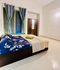 a bedroom with a bed with a blue comforter and a window at Delightful Dwellings 2bhk at 16th floor@kharadi in Pune