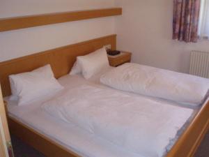 Bett mit weißer Bettwäsche und einem Kopfteil aus Holz in der Unterkunft Reinprecht in Tux