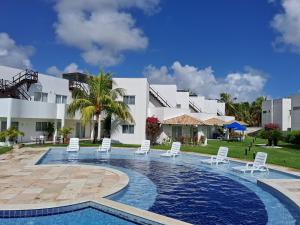 a swimming pool with white chairs and a building at Paraíso de Maracajaú 4 in Maxaranguape