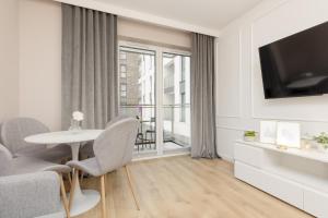 a white living room with a table and a tv at White & Gold Marble Apartment Łódź Fabryczna by Renters in Łódź