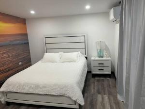 a white bedroom with a bed and a night stand at Huellas in Arecibo