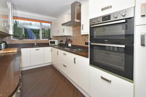 a kitchen with white cabinets and black appliances at Hale View by YourStays in Altrincham