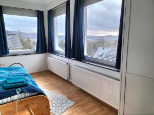 Schlafzimmer mit großen Fenstern und einem Bett mit blauen Vorhängen in der Unterkunft Ferienhaus Weitblick in Bad Pyrmont
