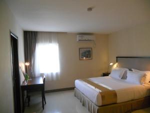 um quarto de hotel com uma cama, uma secretária e uma janela em Plaza Hotel em Dili