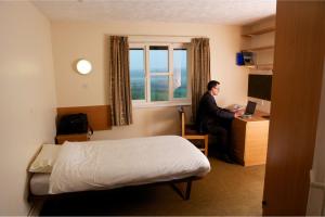 un hombre sentado en un escritorio en una habitación de hotel en University of Essex - Colchester Campus en Colchester