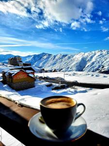 a cup of coffee sitting on a ledge with snow covered mountains at Kai cottage in Gudauri
