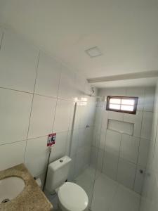 a white bathroom with a toilet and a window at Suítes Vilas do atlântico a 100M da praia in Lauro de Freitas