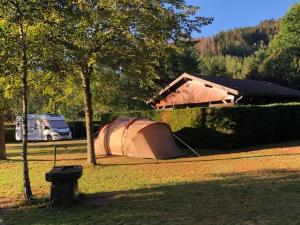 a tent in the grass next to a tree and a house at Camping Pré Vologne in Granges-sur-Vologne